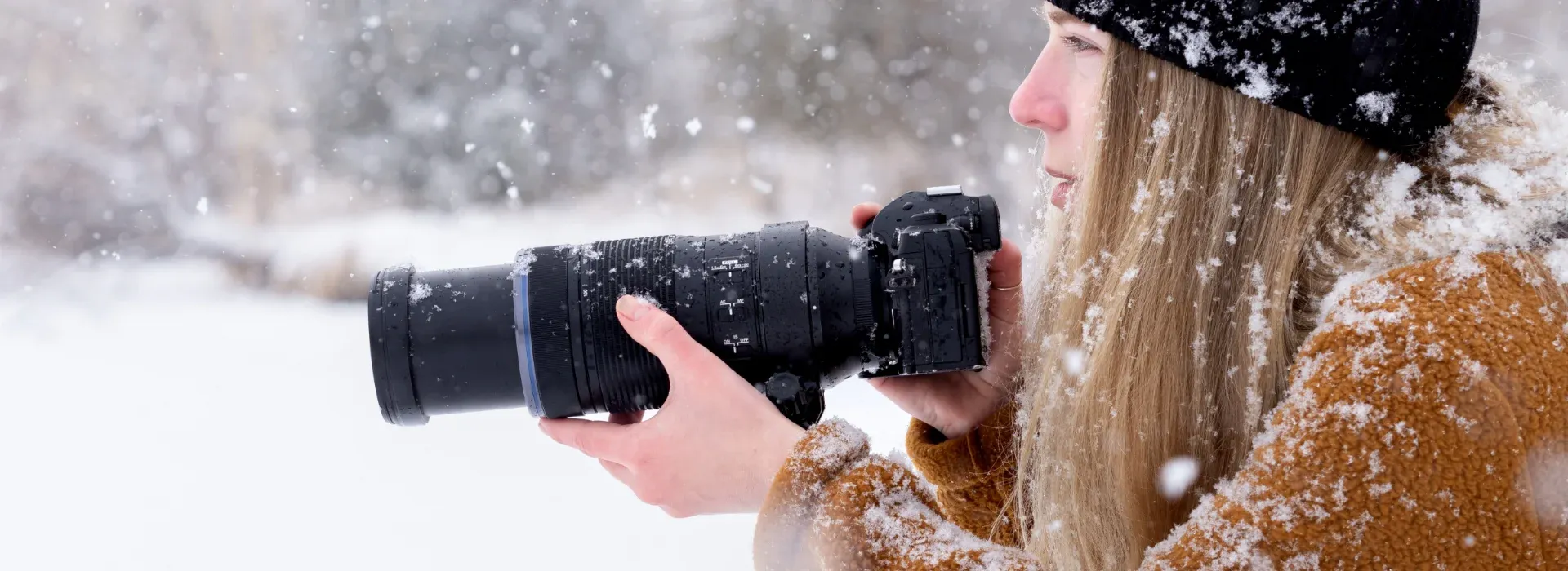 Photo of a camera and lens in a girls hand in a snowy field getting ready to take a photo.