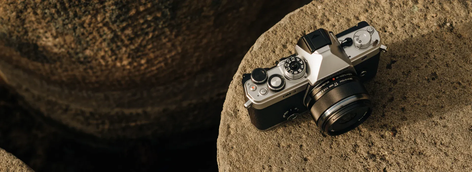 Photo of a om-3 and 17mm lens sitting on a round concrete block.