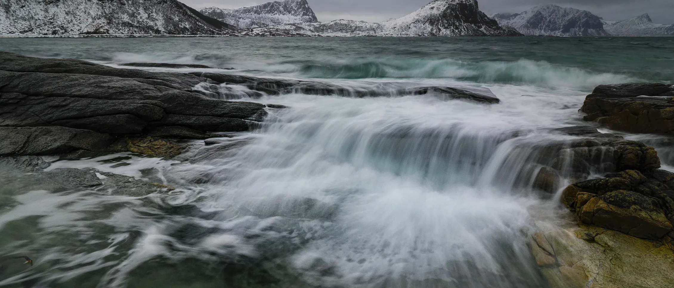 Foto van een korte waterval met overstromend water waarbij een lange sluitertijd is gebruikt om een zacht vervaagd watereffect te creëren, gefotografeerd met de OM SYSTEM OM-3.